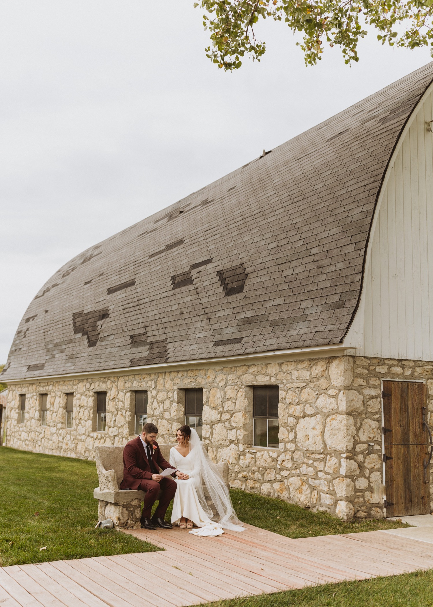 Bride and groom sitting on bench in front of barn, reading notes written to each other